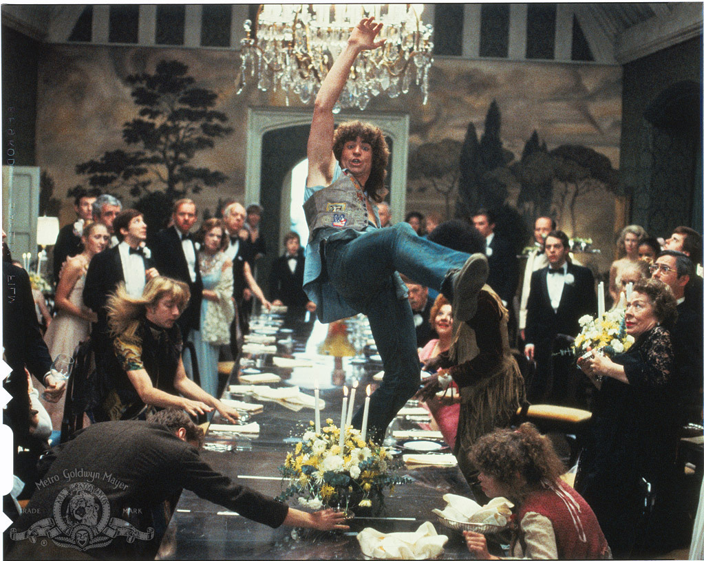 Mann som svinger seg i lysekrone i stort middagsselskap